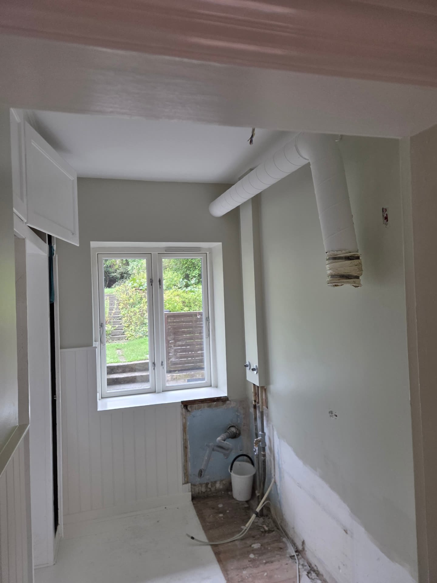 Bryggers under renovering med hvidt vægpanel, grågrøn væg og hvidmalet loft